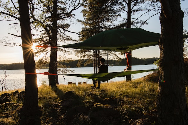 A person sitting on a hammock tent by the lake enjoying the sunrise and the fresh morning breeze